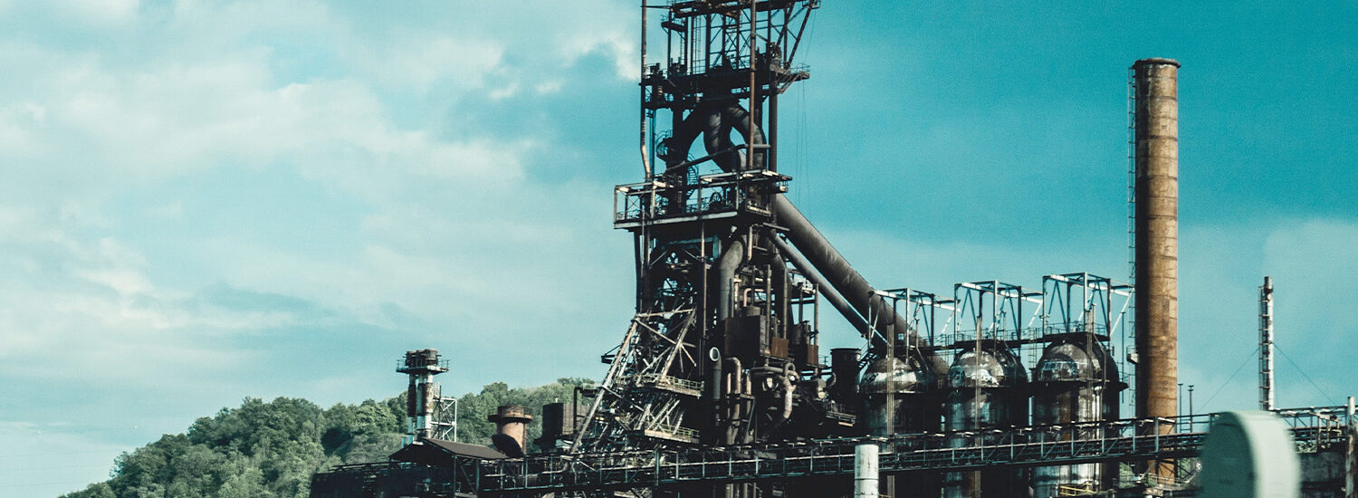 Large industrial manufacturing plant with steel structures, piping, and smokestack under a partly cloudy sky, symbolizing heavy industry, power generation, and industrial automation infrastructure.