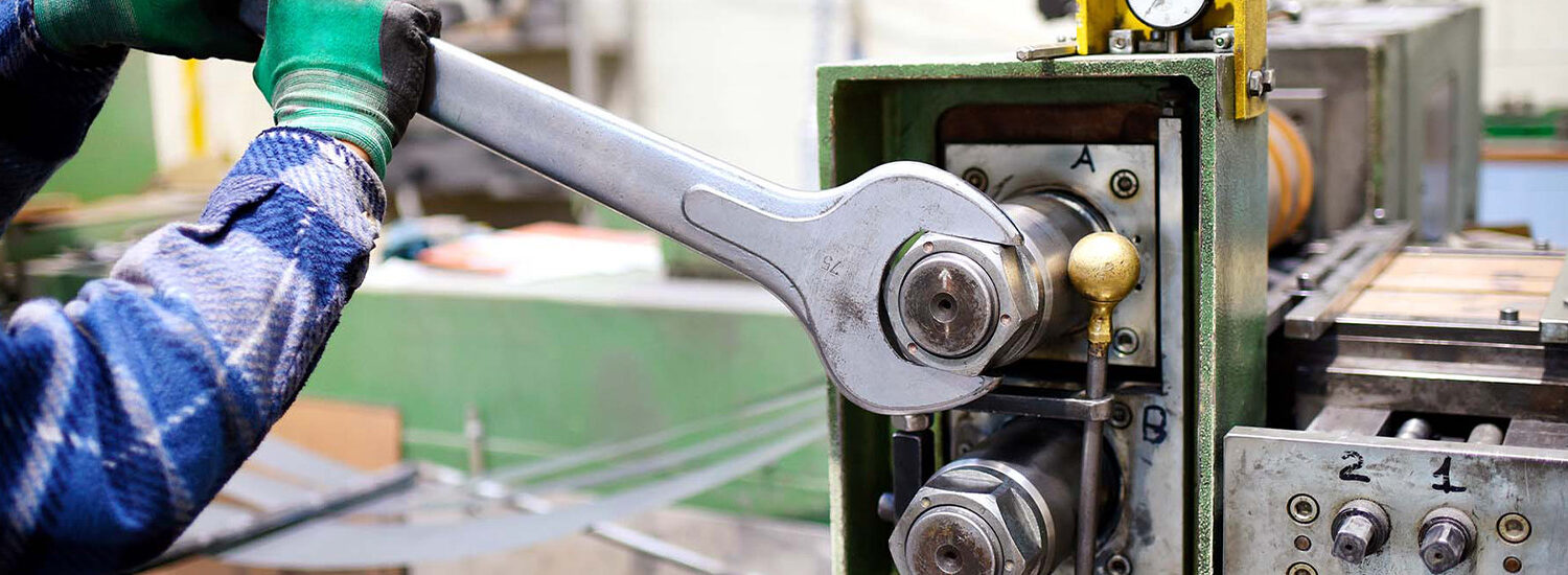 Technician performing precision mechanical maintenance on industrial machinery using a large wrench, showcasing hands-on equipment repair, preventive maintenance, and manufacturing plant operations.